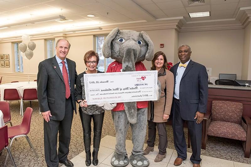 Big Al, University leadership, and 统一的方式 leadership members hold a giant check